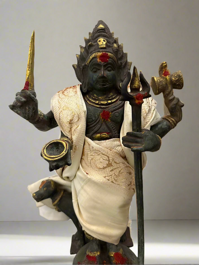 Statue of a deity kaalbhiarav holding a trident and other symbols, with a decorative background.